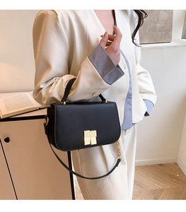 Détail d'un sac carré en cuir noir avec boucle dorée porté avec un blazer blanc élégant