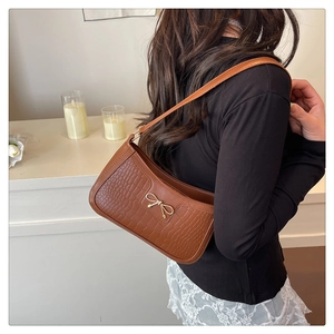 Brown crocodile pattern shoulder bag with a gold bow accent worn by a model