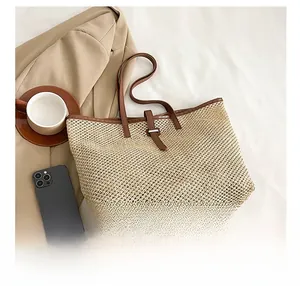 Top view of beige woven tote bag with brown leather handles and casual office accessories
