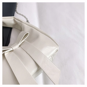 Close-up of cream glossy leather handbag featuring a large bow and silver chain strap