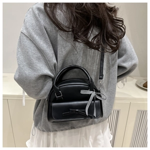 Detail of a black semi-round crossbody bag with ribbon bow decoration on model