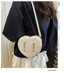 Detail of white heart-shaped crossbody bag with crocodile texture and silver chain strap