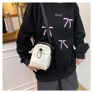 Close-up of cream drawstring crossbody bucket bag with black strap on a model