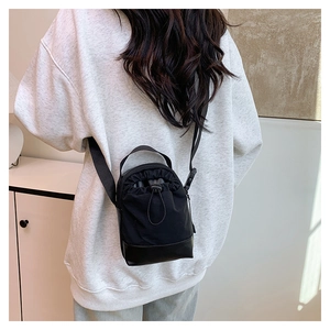 Detail of black nylon crossbody bag with drawstring closure and leather reinforced bottom