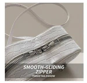 Detailed close-up of the smooth silver dual metal zippers on white croc-embossed leather