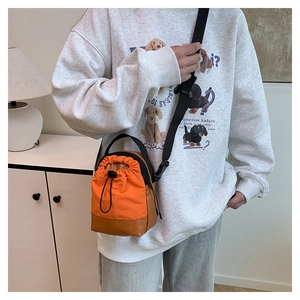 Detail of a dual-color drawstring crossbody bucket bag worn by a lifestyle model