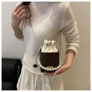Detail of a brown croc-effect mini bucket bag with pearl handle and golden chain