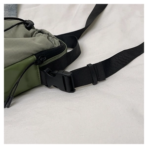 Detail of green tactical crossbody bag with buckle, nylon strap, and drawstring closure