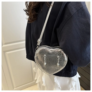 Close-up of silver heart-shaped crossbody bag with crocodile pattern and metal chains
