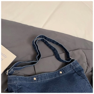 Détail d'un sac cabas en denim bleu foncé avec surpiqûres blanches et rivets en métal