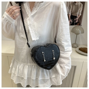 Detail of a heart-shaped crossbody bag featuring black crocodile pattern and silver chains