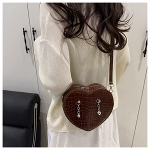 Detail of a dark brown heart-shaped bag with crocodile texture and silver chain charms