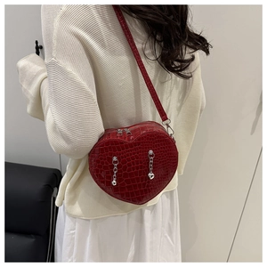 Red heart-shaped crocodile pattern crossbody bag with silver chains on white sweater