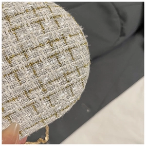 Close-up of white tweed texture with gold metallic threads and a slim metal chain