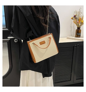 Détail du sac cabas en paille tissée avec garniture en cuir brun et chaîne dorée