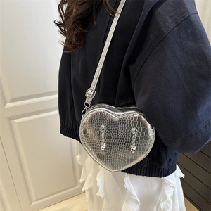 Silver heart-shaped crocodile pattern crossbody bag with chain charms worn by a model
