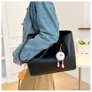 Close-up of black leather tote bag featuring a cute pink furry keychain for daily commute