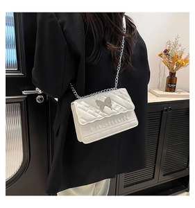 Detail of white quilted crossbody bag with silver butterfly ornament and chain strap
