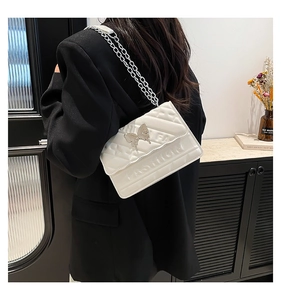 Close-up of white quilted crossbody bag featuring silver butterfly buckle and chain strap