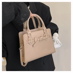 Detail van beige crossbodytas met lederen strikdecoratie en gouden gesp-accenten