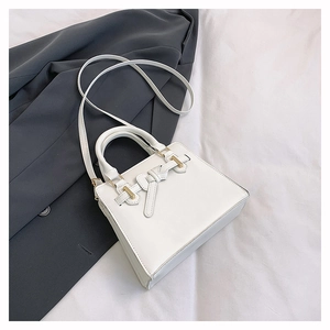 Détail d'un sac à bandoulière blanc avec un nœud décoratif en cuir et des boucles dorées