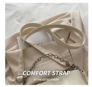 Detail of cream shoulder bag featuring cracked patent leather texture and silver chain strap