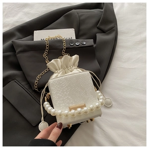 Detail of white crocodile embossed bucket bag with pearl handle and golden chain