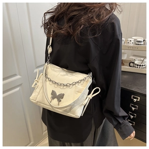 Detail view of cream shoulder bag featuring silver butterfly charm and chain decoration