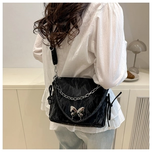 Detail of glossy pleated leather shoulder bag with silver butterfly metal buckle and chain