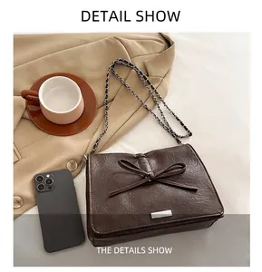 Detail view of dark brown faux leather crossbody bag with bow accent and chain strap