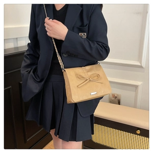 Detail of beige crossbody bag with leather bow decoration and silver chain strap