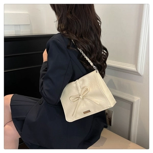 Detail of cream shoulder bag with pleated texture, leather bow, and metal chain strap