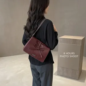 Close-up of a burgundy chain bag with a decorative bow and textured PU leather finish