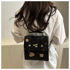 Detail of a black mini backpack with yellow embroidery and patches worn on a white shirt
