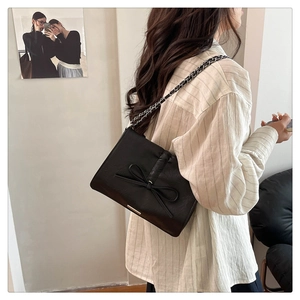 Side view of black faux leather shoulder bag with bow detail on female model