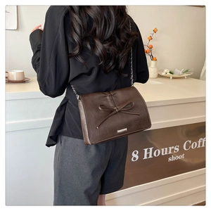 Detail view of brown leather bag with bow accent and silver chain strap on model