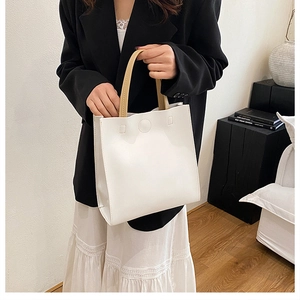 Chic white commuter tote bag featuring light brown handles and a magnetic closure detail