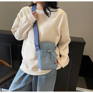 Detail of light blue nylon crossbody bag with adjustable drawstring and red side label
