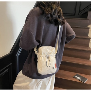 Detailed back view of a beige nylon crossbody bag with drawstring pocket and adjustable strap