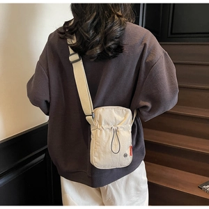 Detail of off-white crossbody bag featuring drawstring front pocket and adjustable strap