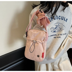 Detailed view of a light pink crossbody bag with drawstring pocket and woven strap