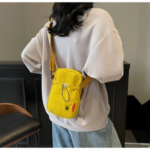 Detail of yellow canvas crossbody bag featuring decorative drawstring and side label