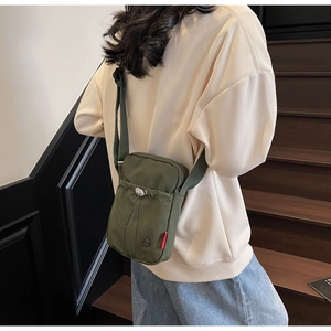 Rear view of a dark green canvas mini crossbody bag worn by a model on a staircase