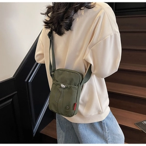 Detailed back view of a dark green canvas crossbody bag on a casual spring outfit