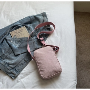 Close-up of a pink mini crossbody phone bag with adjustable strap on white bedding