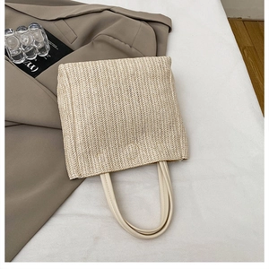 Close-up of woven straw handbag with cream leather handles and herringbone pattern