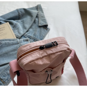 Flat lay of pink nylon crossbody bag with drawstring design and blue denim jacket