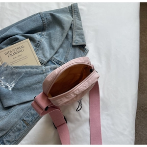 Detail view showing internal compartment of a pink nylon crossbody bag on a white bedsheet