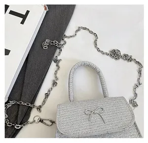 Close-up of silver-grey woven bag with metal bow buckle and chain shoulder strap