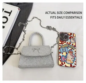 Mini trapezoid glitter crossbody bag with metallic bow detail beside a mobile phone
